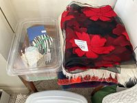 Photo showing the blankets stacked on a small chair and clear plastic box containing various candle boxes, highlighting the mix of textiles and candle packaging.