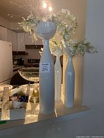 Three white porcelain vases of varying heights standing on countertop with artificial flowers