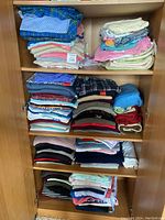 Full view of wooden cabinet shelves stacked with neat piles of folded casual clothing in multiple colors and patterns.