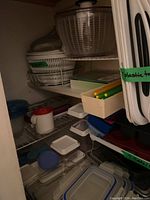 Multiple kitchen items stored on wire shelves including salad spinners, trays, containers, and trivets.