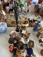Photo showing overall lot with metal male figure sculpture, wooden elephant, ceramic vase, blue and white jar, and assorted decorative items on table