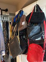 Eight purses and handbags hanging on a door, showing different colors, materials, and designs including black, red, and brown bags.