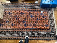Full view of the hand woven rectangular rug on a wood floor showing geometric patterns and border designs.