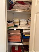 Closet shelf with multiple stacked blankets on the top shelf and assorted towels folded below.