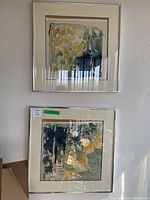 Photo showing two framed watercolour paintings hung vertically on a wall, both featuring abstract compositions in muted tones.
