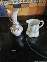 Two porcelain creamers: One Lefton China hand-painted with floral relief and gold handle, and one Hanley of England J & G Meakin floral porcelain creamer with scalloped rim.