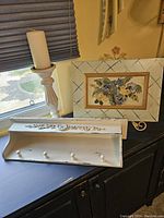 Tall, distressed white wooden candle holder with pillar candle on table near window