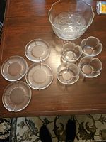 Shot of the full dessert set showing the large etched floral glass bowl, 4 flower-shaped bowls and 4 small plates arranged on wooden table.