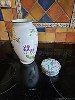 Porcelain floral vase and world map trinket box on black stovetop.