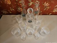 Set of 4 highball glasses, 3 rock glasses, 2 pony glasses, and 3 crystal decanters on a table with patterned wallpaper background.