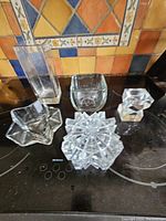 All five glass pieces shown together on a stove top with decorative tile background. Pieces include star-shaped bowl, square bowl, starburst bowl, tall rectangular vase, and small chunky square container.