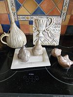 Group shot of all pottery pieces arranged on a stovetop including vase, pears on dish, birds, and decorative tile