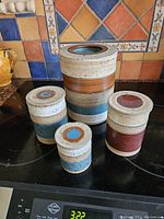 Four Denby ceramic storage jars arranged by size, showing textured colored bands and lids on a kitchen stovetop.
