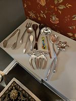 Photo of all 12 serving pieces including metal and wooden utensils arranged on a white table, captured to show full lot contents.