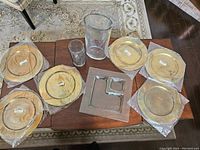 Photo of six brass charger plates, two glass vases, and a square glass serving tray on a wooden table.