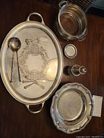 Large oval serving platter along with two smaller round serving bowls, smaller utensils, and coasters arranged on wooden table