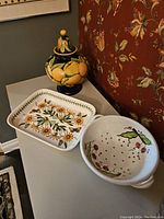 Photo showing the complete pottery collection of three items on white surface against floral wallpaper.