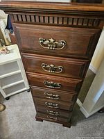 Tall wooden high boy dresser with five drawers, brass handles, and carved details.
