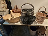Five large woven picnic baskets displayed on a table, showing variety of shapes and colors