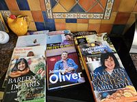 Overview of 11 hard cover cookbooks featuring Ina Garten, Jamie Oliver, Tyler Florence, Martha Stewart, and Food Network chefs, arranged on kitchen counter.