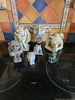 Seven gargoyle statues displayed on stovetop with tile backsplash, showing variety of designs and sizes.
