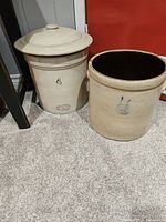 Two cream-colored antique pottery crocks, one with lid marked '4' and one open topped with painted blue design.