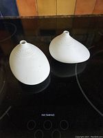 Photo showing two white Rosenthal bud vases on a black surface, featuring elliptical shapes and textured circular pattern near openings.