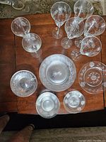 Top-down view of the crystal plates and stemmed wine glasses on a wooden table, showing detailed floral etching on both glass and plates.