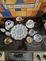 Top view of the tableware items on a black stovetop surface with colorful tiled backsplash, showing all items arranged for inspection.