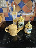 Four assorted decorative ceramic oil and vinegar vessels with olive motifs arranged on stove top against colorful tile backsplash