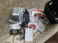 Layout of Dr. Ho's Pain Therapy System Pro with device, electrode pads, power adapter, carrying pouches, manuals, and DVD on carpeted surface.