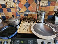 Full view of kitchen package including grill pan, roaster, taco rack, cutting board, pizza stone, and asparagus steamer on countertop with tiled backsplash