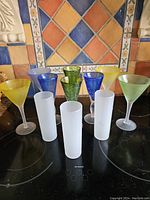 Full set of 11 colorful 1980s drinking glasses showing variety in shapes, colors and textures.