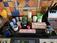 Photo showing a variety of candles on a stove top including pillar candles, votives, lantern holders, and green decorative holder.