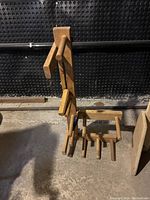 Front view of two handmade wooden inkle looms with pegs and dowels. Larger loom leaning back with some pegs missing.