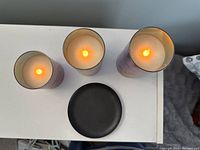 Top-down view showing three battery operated candles with illuminated LED flames and the black metal holder in center.
