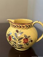 Side view of the yellow ceramic pitcher with hand painted floral motif and handle