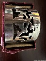 Close-up image of the antique silver napkin ring showing cut-out floral pattern and hallmark 'JACOBS ENGLAND'.
