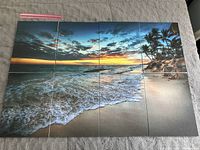 Eight soundproofing tiles arranged to form the full sunset beach mural showing ocean waves, sandy beach, rocks, and palm trees under a colorful sunset sky.