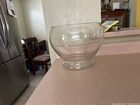 Clear view of the round, pedestal-style clear glass punch bowl placed on a kitchen counter.