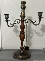 Front view of a two-arm brass and wood candle holder with attached brass snuffer.