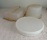 Three vintage Tupperware cake, cookie and pie takers together on a beige cloth, showing their size and shape.
