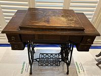 Overview photo of antique sewing machine cabinet closed showing wood surface and treadle base.