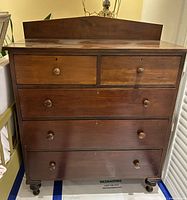 Full front view of the wooden dresser showing five drawers with round wooden knob handles and keyholes.
