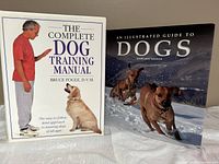 Two hardcover dog-themed books side by side: 'The Complete Dog Training Manual' and 'An Illustrated Guide to Dogs'