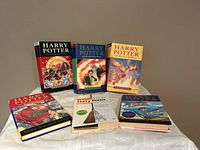 Six hardcover Harry Potter books and two softcover books arranged on a cloth surface, showing colorful illustrated covers in excellent condition.