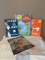 Four children's books arranged with The Lorax in the center front, The Cat in the Hat and Green Eggs and Ham behind it, and The Velveteen Rabbit in front lying flat, showing colorful illustrated covers.