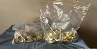 Two sealed clear plastic bags containing multiple brass cabinet handles and knobs placed on a gray surface.