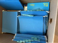 Photo of multiple blue hanging file folders in a box with tabs visible on folders.