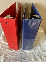 Side view of red and blue 3 inch binders showing metal rings and condition of covers